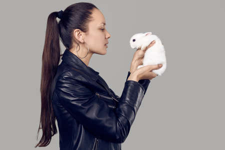 Portrait of gorgeous latin women in fashion leather jaket with cute little rabbit on gray studio backgroundの写真素材
