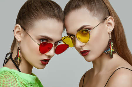 Portrait of two elegant glamor hipster twin girls in fashion neon green dresses with sunglasses posing on gray background in studioの写真素材