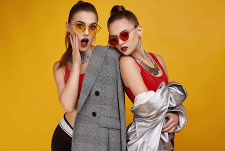 Portrait of two elegant glamor hipster twin girls in fashion red top, black shorts and sunglasses posing on colorful background in studioの写真素材