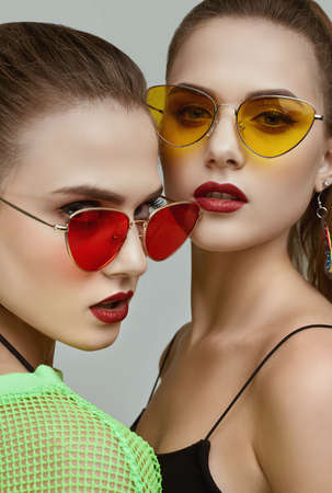Portrait of two elegant glamor hipster twin girls in fashion neon green dresses with sunglasses posing on gray background in studioの写真素材