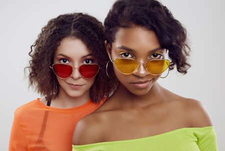 Portrait of two young beautiful hipster girls in trendy colorful summer clothes and bright...