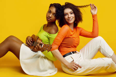 Portrait of two young beautiful hipster girls in trendy colorful summer clothes playing the small...
