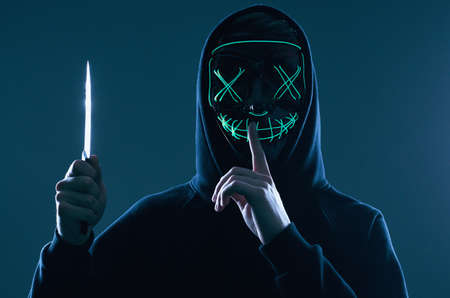 Portrait of an anonymous criminal man with big kitchen knife in a black hoodie hiding his face...