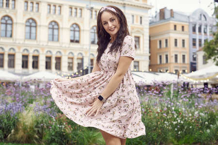 Portrait of a young beautiful bright girl in a summer dress laughing and walking in the city park of...