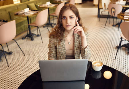 Portrait of confident young businesswoman in smart casual wear drinks coffee and working on laptop...