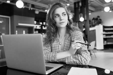 Portrait of confident young businesswoman in smart casual wear makes notes in a notebook in a coffee...