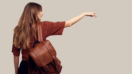 Portrait of young beautiful woman with backpack ready to travel. Smiling student girl going on a vacation. Isolated on gray background.の写真素材