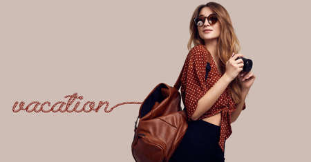 Portrait of young beautiful woman with backpack and camera ready to travel. Smiling student girl going on a vacation. Isolated on gray background.の写真素材