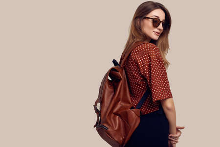 Portrait of young beautiful woman with backpack ready to travel. Smiling student girl going on a vacation. Isolated on gray background.の写真素材
