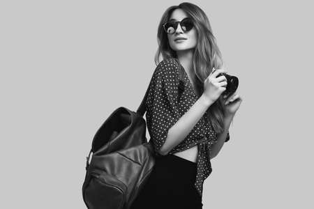 Portrait of young beautiful woman with backpack and camera ready to travel. Smiling student girl going on a vacation. Isolated on gray background.の写真素材