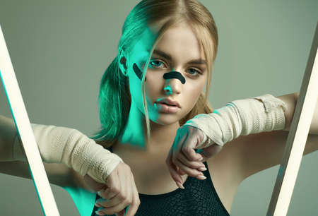 Vivid portrait of strong beautiful girl with blonde hair, sports figure, confident look and fists in protective boxing bandages posing on colorful neon light backgroundの写真素材