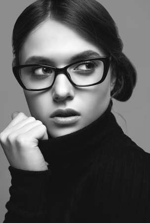 Portrait of cute student girl wearing black turtleneck sweater and stylish eyeglasses posing on gray...