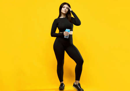 Portrait of a gorgeous body positive Latin woman in a black sports suit with a bottle of water...