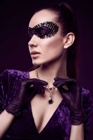 Portrait of charming elegant brunette woman in beautiful purple dress, sequins mask and black gloves posing with a stolen diamond necklaceの写真素材