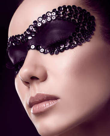 Close-up portrait of charming elegant brunette woman in sequins mask posing on black background in studioの写真素材