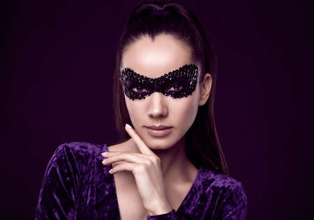 Portrait of charming elegant brunette woman in beautiful purple dress and sequins mask posing on black background in studioの写真素材