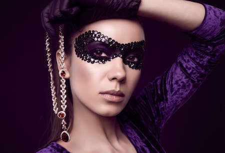 Portrait of charming elegant brunette woman in beautiful purple dress, sequins mask and black gloves posing with a stolen diamond necklaceの写真素材