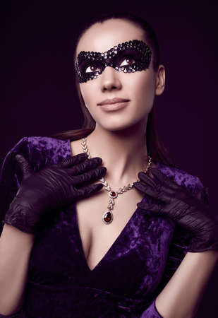 Portrait of charming elegant brunette woman in beautiful purple dress, sequins mask and black gloves posing with a stolen diamond necklaceの写真素材