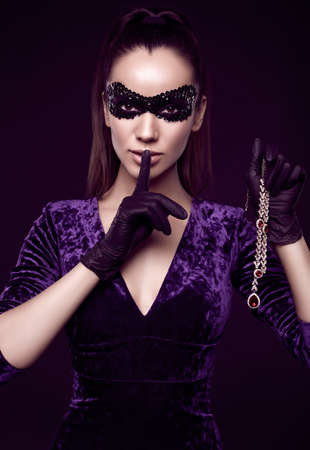 Portrait of charming elegant brunette woman in beautiful purple dress, sequins mask and black gloves posing with a stolen diamond necklaceの写真素材