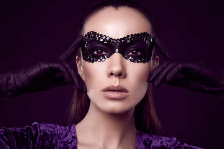 Close-up portrait of charming elegant brunette woman in sequins mask and gloves posing on black background in studioの写真素材