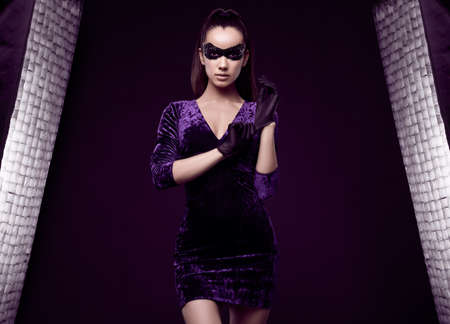 Portrait of charming elegant brunette woman in beautiful purple dress and sequins mask glove up on black background in studioの写真素材