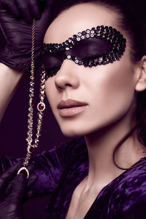 Portrait of charming elegant brunette woman in beautiful purple dress, sequins mask and black gloves posing with a stolen diamond necklaceの写真素材
