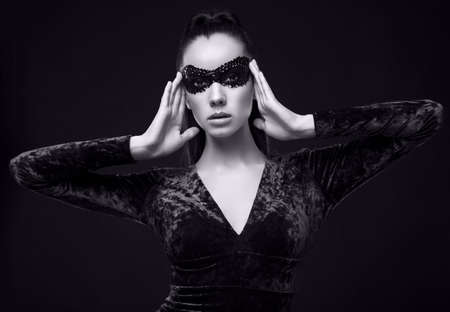 Portrait of charming elegant brunette woman in beautiful purple dress and sequins mask posing on black background in studioの写真素材