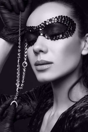 Portrait of charming elegant brunette woman in beautiful purple dress and sequins mask posing on black background in studioの写真素材