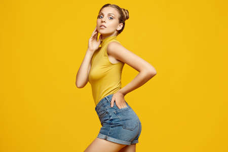 Positive portrait of gorgeous blonde hipster woman model with curly hair posing on colorful yellow...