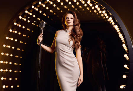 Portrait of gorgeous singer woman in elegant dress with retro microphone on restaurant stage...