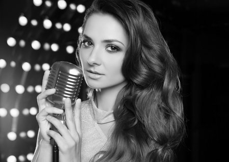 Portrait of gorgeous singer woman in elegant dress with retro microphone on restaurant stage spotlights background.の写真素材