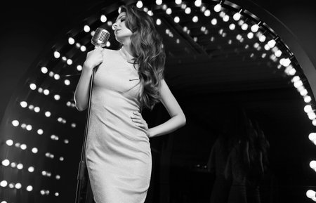 Portrait of gorgeous singer woman in elegant dress with retro microphone on restaurant stage spotlights background.の写真素材