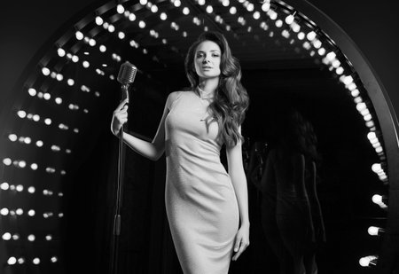 Portrait of gorgeous singer woman in elegant dress with retro microphone on restaurant stage spotlights background.の写真素材