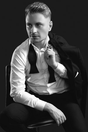 Portrait of handsome blond man in elegant tuxedo and bow tie posing on black studio backgroundの写真素材