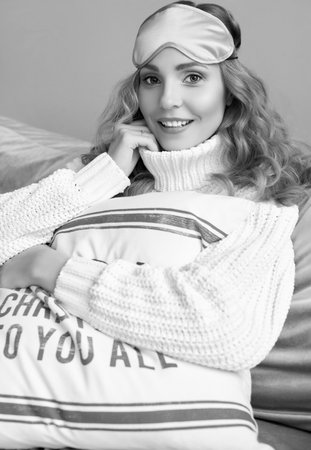 Portrait of gorgeous blonde woman in white woolen sweater and eyemask smiling in light cozy interior.の写真素材