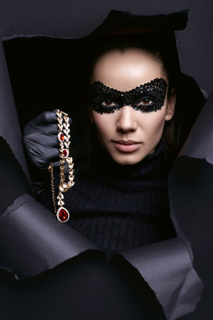 Portrait of charming elegant brunette woman in turtleneck sweater and sequins mask with black gloves posing with a stolen diamond necklaceの写真素材