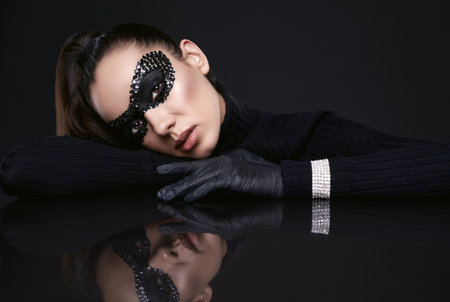 Portrait of charming elegant brunette woman in black turtleneck sweater and sequins mask posing on a mirrored surface in studioの写真素材
