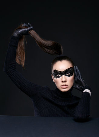 Portrait of charming elegant brunette woman in turtleneck sweater and sequins mask posing on black background in studioの写真素材