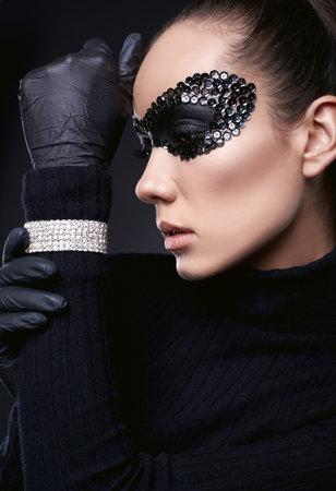 Portrait of charming elegant brunette woman in turtleneck sweater and sequins mask posing on black background in studioの写真素材