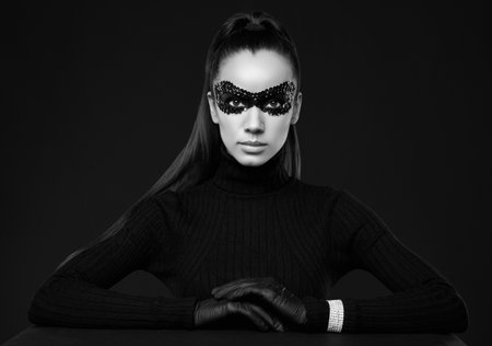 Portrait of charming elegant brunette woman in turtleneck sweater and sequins mask posing on black background in studioの写真素材