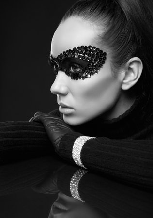 Portrait of charming elegant brunette woman in black turtleneck sweater and sequins mask posing on a mirrored surface in studioの写真素材