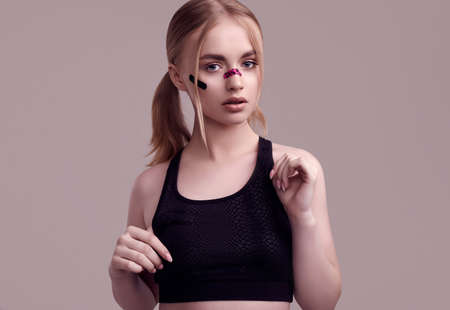 Sensual portrait of beautiful blonde girl with glamor plasters on her face posing at studio...