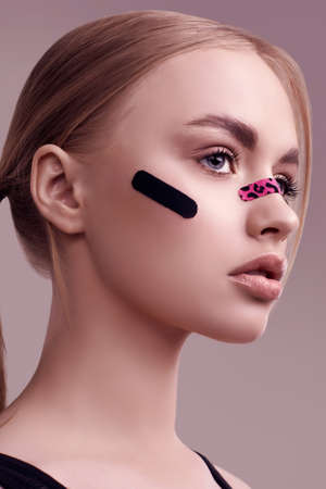 Sensual portrait of beautiful blonde girl with glamor plasters on her face posing at studio backgroundの写真素材