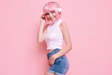 Portrait of gorgeous bright sexy hipster girl with pink hair enjoys the music in headphones on...