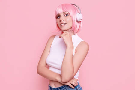 Portrait of gorgeous bright sexy hipster girl with pink hair enjoys the music in headphones on colorful backgroundの写真素材