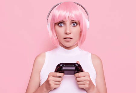 Portrait of gorgeous happy sexy gamer girl with pink hair playing video games using joystick on colorful background in studioの写真素材