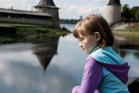 blonde girl looks thoughtfully at the river on the background of the Pskov Kremlinの写真素材