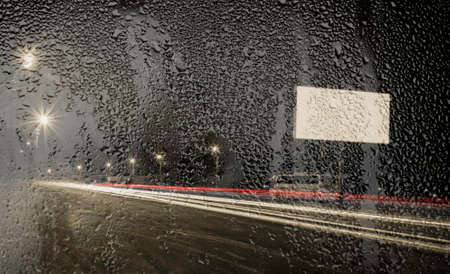night view of the street through the glass with raindropsの写真素材