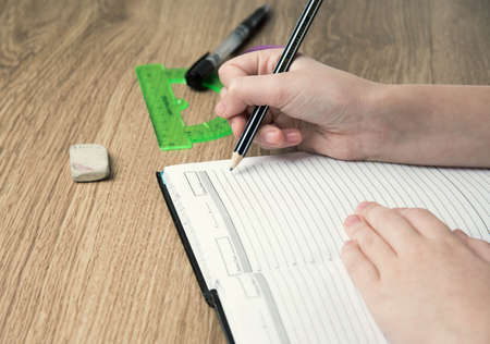 child hands writing in the album on wooden table