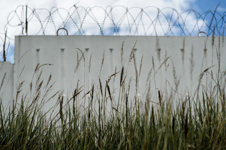 grass with concrete fence with barbed wire and sky with clouds